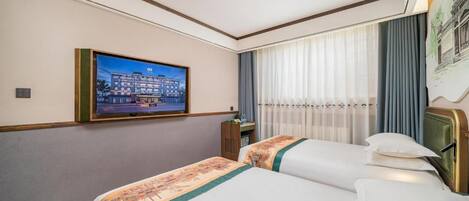 Una habitación de hotel con dos camas, un televisor en la pared y una ventana con cortinas.