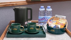 A tray with a black electric kettle, two water bottles, two green tea cups, and a basket of packaged snacks. - Nostalgia S Hotel(beijing Tianqiao (Beijing)