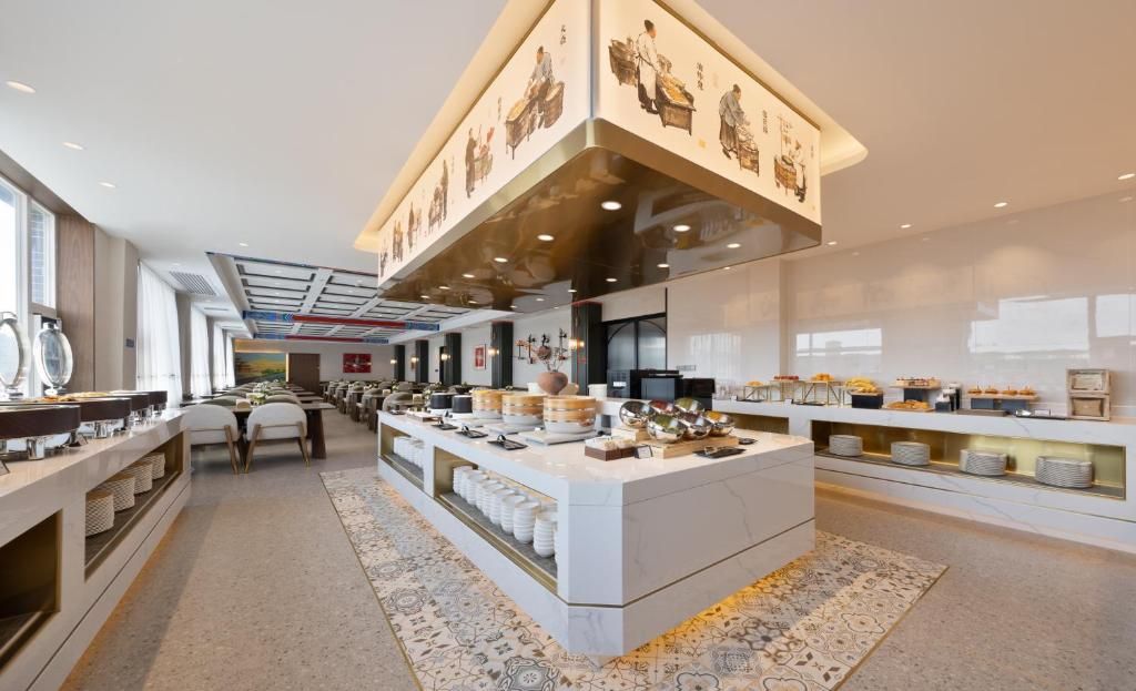 A modern hotel lobby with a central buffet area, seating arrangements, and a large window providing natural light.