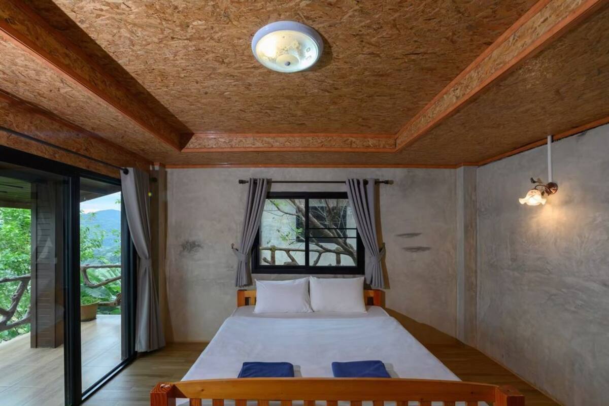 Une chambre avec un grand lit, une fenêtre avec des rideaux, un luminaire au plafond et un balcon avec vue.