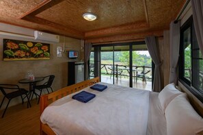A hotel room with a bed, a desk with a chair, a TV, and a balcony with outdoor seating. - Mon View Ngarm (Chiang Mai)