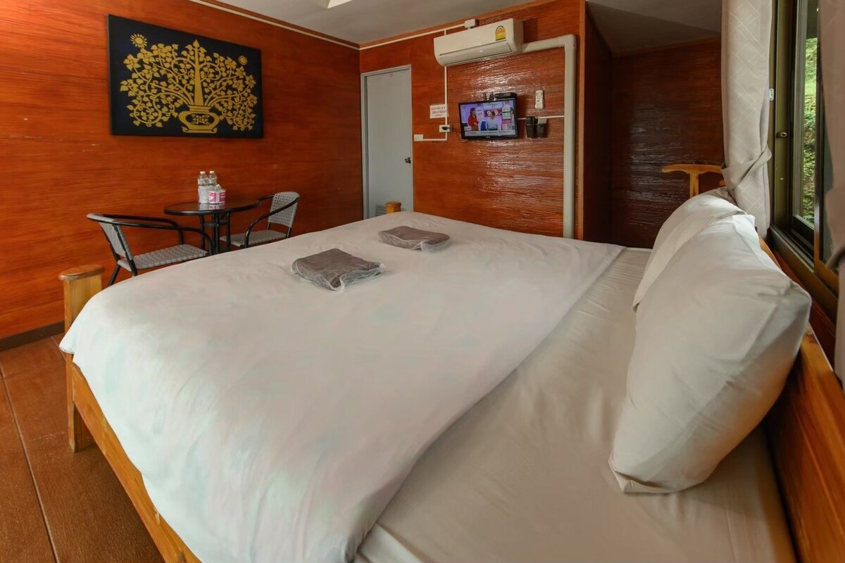 Una camera d'hotel con un letto, una televisione, un tavolino con sedie e un elemento decorativo a parete.