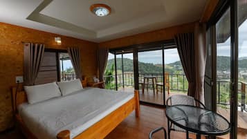 A bedroom with a wooden bed, a balcony with a table and chairs, and a view of the landscape.