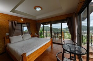 A bedroom with a wooden bed, a balcony with a table and chairs, and a view of the landscape. - Mon View Ngarm (Chiang Mai)