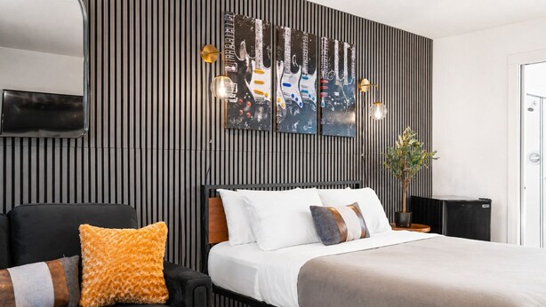 Ein modernes Schlafzimmer mit einem Bett, einem schwarzen Sessel, einem an der Wand montierten Fernseher und einer Topfpflanze.