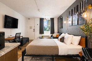 Une chambre d’hôtel moderne, équipée d’un lit, d’un bureau, d’une télévision et ornée d’œuvres d’art sur les murs.