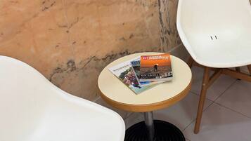 A corner with a white chair, a small round table with magazines, and a marble wall.