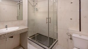 Un baño con ducha envuelta en vidrio, lavabo con encimera de granito y retrete.