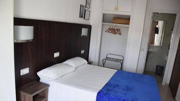 A single bed with a white and blue bedspread, a wooden nightstand, a wardrobe with hanging space, and a mirror.