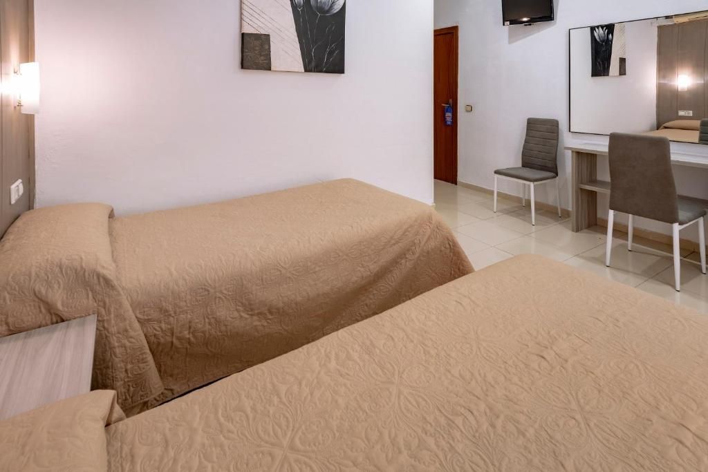 A room with two beds, a desk, a chair, a TV, and artwork on the walls.