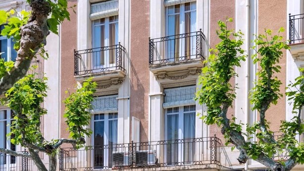 Un edificio de varios pisos con balcones, ventanas y árboles.
