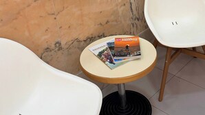 Un rincón con una silla blanca, una mesita redonda pequeña con revistas y una pared de mármol.