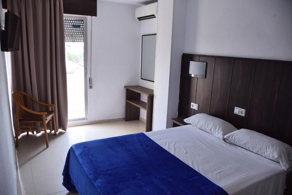A hotel room with a bed, a desk, a chair, a mirror, and a window with curtains.