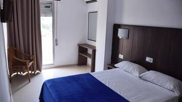 A hotel room with a bed, a desk, a chair, a mirror, and a window with curtains.