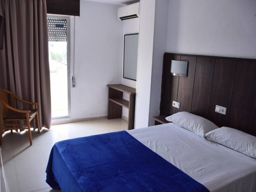 A hotel room with a bed, a desk, a chair, a mirror, and a window with curtains.