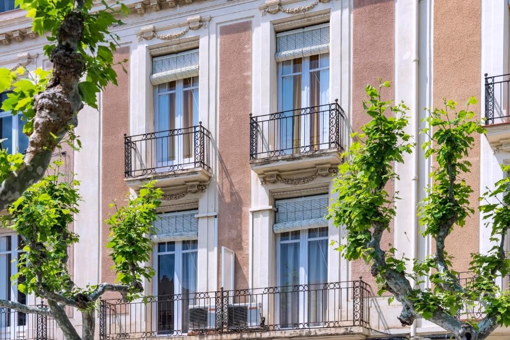 A multi-story building with balconies, windows, and trees.