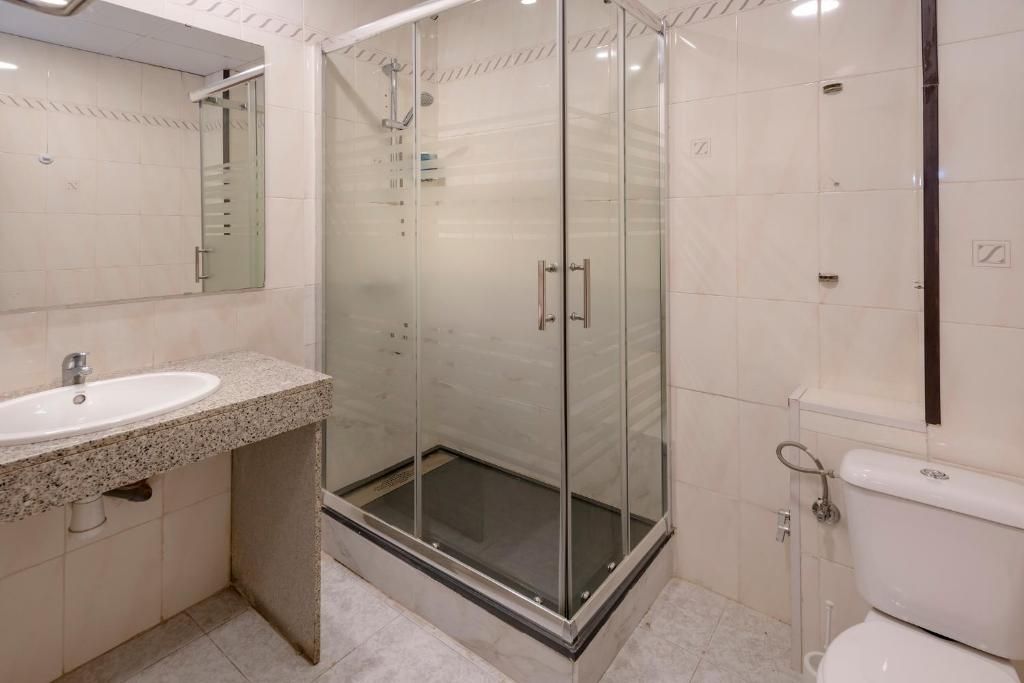 Un baño con ducha envuelta en vidrio, lavabo con encimera de granito y retrete.