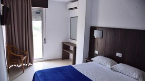 Una habitación de hotel con cama, escritorio, silla, espejo y ventana con cortinas.