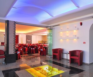 Un moderno vestíbulo de hotel con separadores de vidrio, asientos rojos y una llamativa lámpara decorativa en el centro.