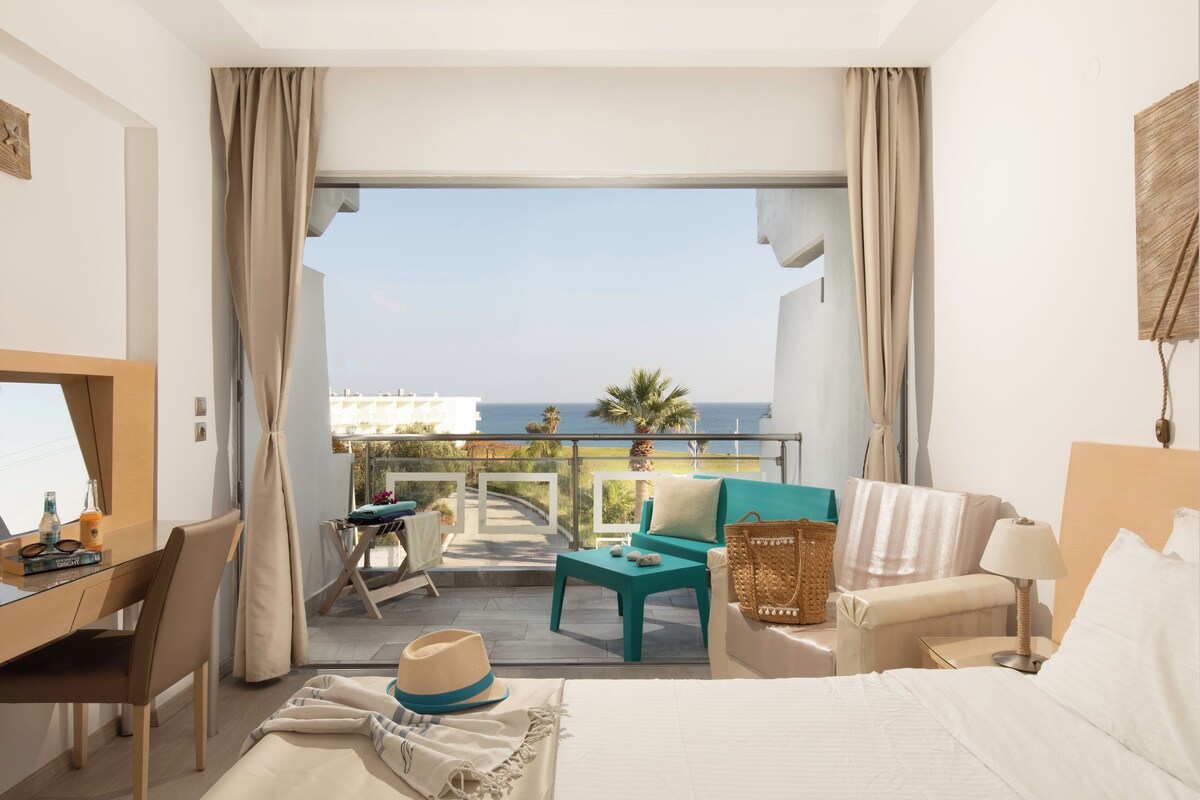 Ein Hotelzimmer mit Balkon, Schreibtisch, Bett und Meerblick.