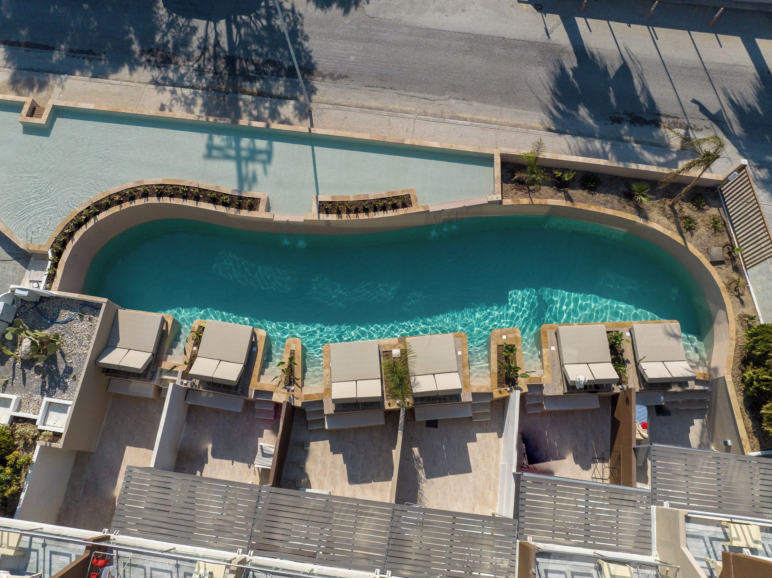Vue aérienne d’une piscine avec des chaises longues et une terrasse en béton.