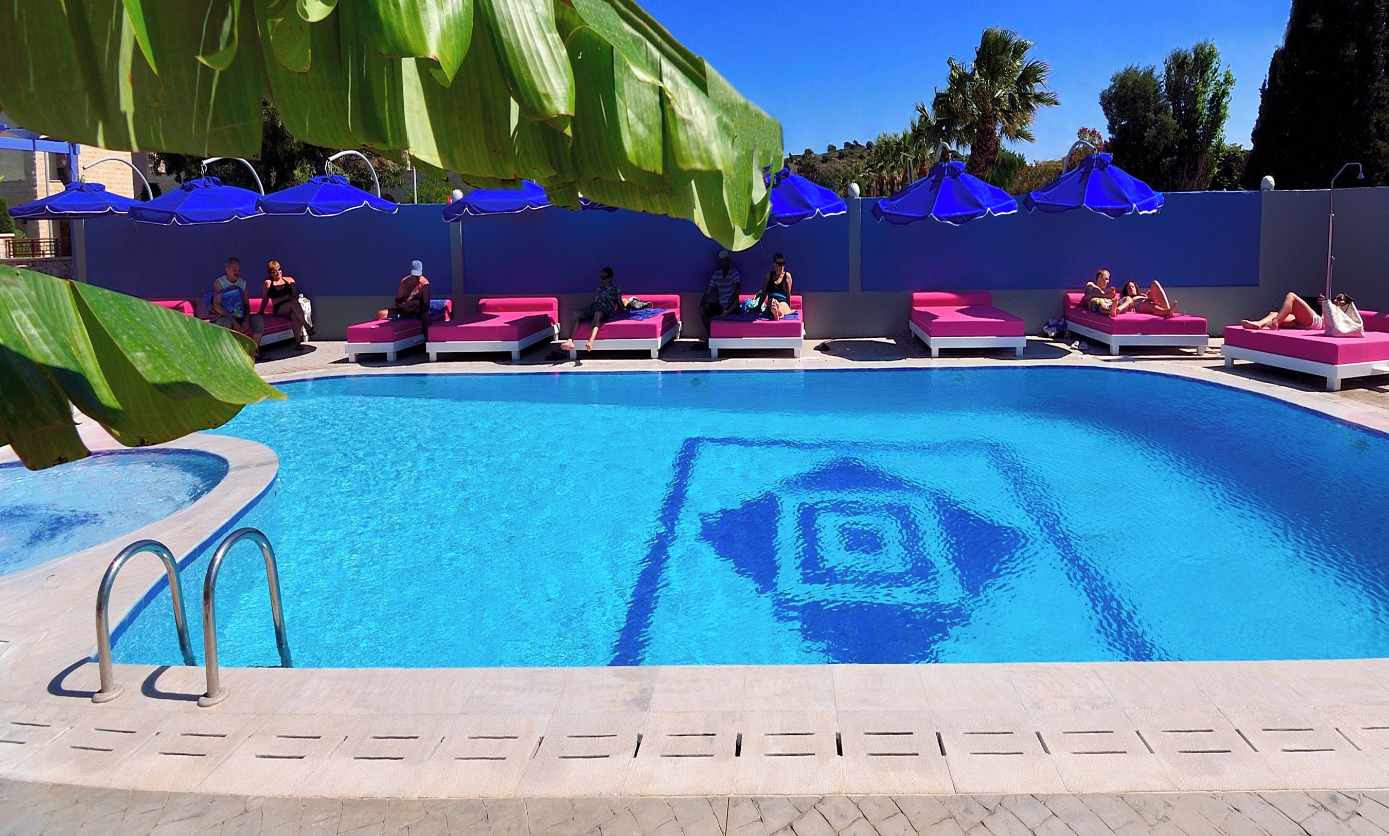 A pool with pink lounge chairs and blue umbrellas.