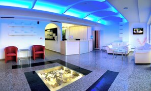 Eine moderne Lobby mit Empfangstresen, Sitzgelegenheiten und einem dekorativen Glastisch.