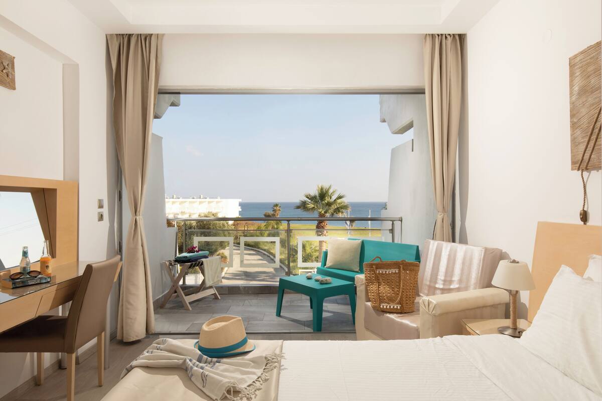 Ein Hotelzimmer mit Balkon, Schreibtisch, Bett und Meerblick.