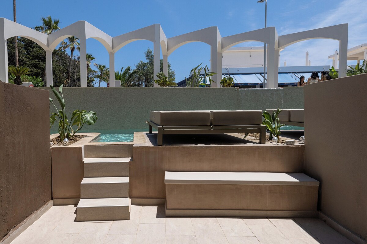 Área à beira da piscina com um banco, degraus e vista para o mar.
