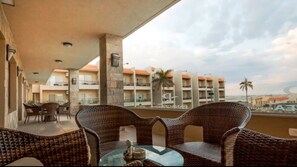 A balcony with wicker furniture and a table, overlooking a building with multiple balconies and palm trees. - Panacea Suites Hotel (Alexandria)
