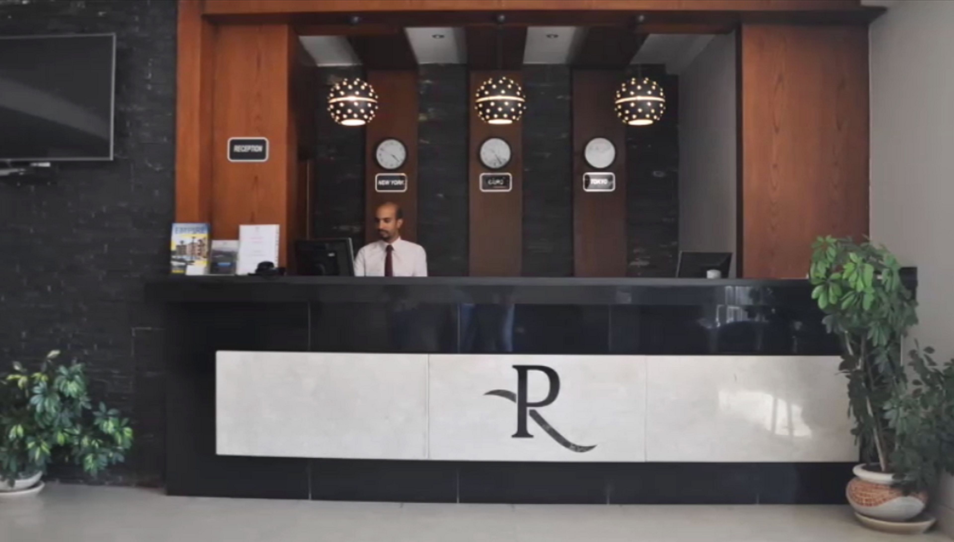 A reception desk with a sign indicating 'Reception,' three clocks above it, and a logo with a capital 'R' on the wall.