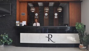 Una recepción con un cartel que indica 'Reception', tres relojes encima y un logotipo con una 'R' mayúscula en la pared.