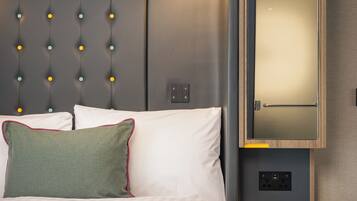 Habitación de hotel con cama, mesita de noche, espejo y lámpara de pared.