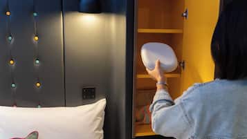 Eine Person legt ein Kopfkissen auf ein Bett mit Kopfteil, das eine Leuchte und eine an der Wand befestigte Bedieneinheit hat.