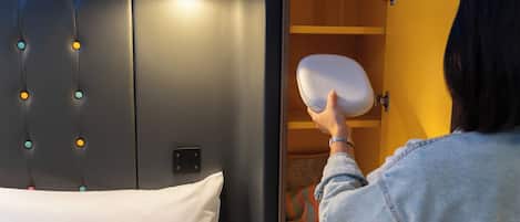 Eine Person legt ein Kopfkissen auf ein Bett mit Kopfteil, das eine Leuchte und eine an der Wand befestigte Bedieneinheit hat.