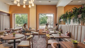 A modern cafe with round tables, cushioned chairs, and large windows offering a view of the street. - Point A Hotel Edinburgh, St Andrew Square (Edinburgh)