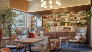 A cozy reading area with leather chairs, a bookshelf, and a large window. - Point A Hotel Edinburgh, St Andrew Square (Edinburgh)