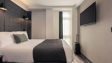 A hotel room with a bed, a flat-screen TV mounted on the wall, and a suitcase on the floor.