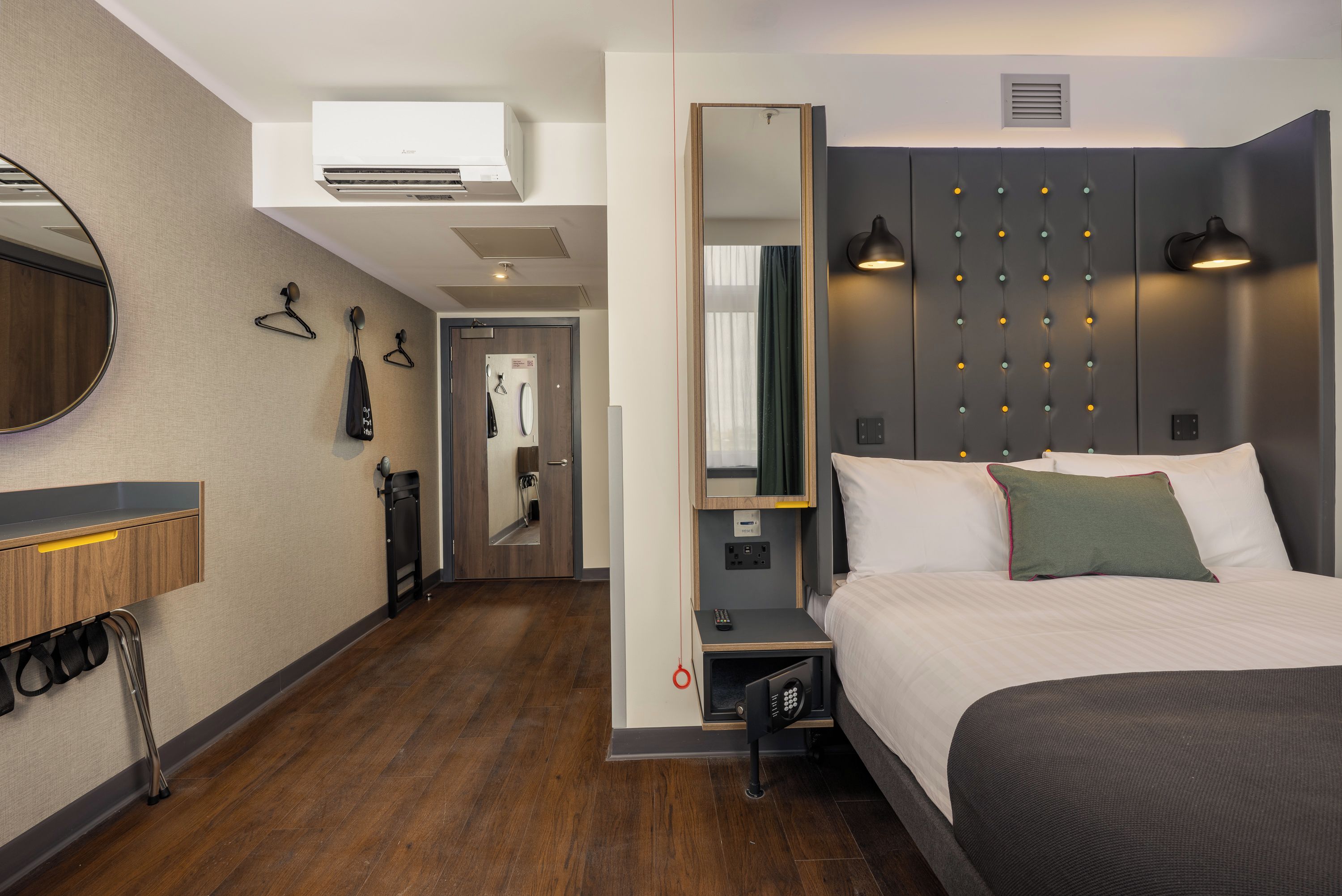 Une chambre d’hôtel comprenant un lit, une table de chevet, un miroir, une armoire et une porte de salle de bain.