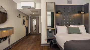 A hotel room with a bed, bedside table, mirror, wardrobe, and a bathroom door.