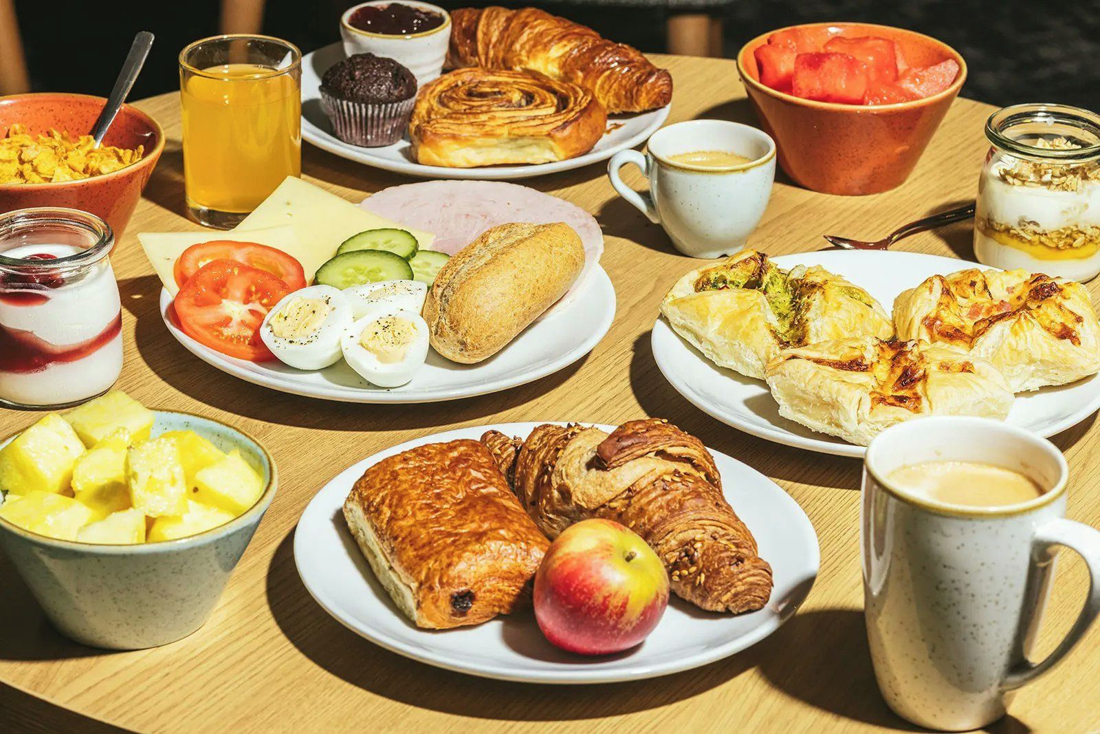 Una mesa de desayuno con diversas opciones de comida, como cruasanes, huevos y fruta.