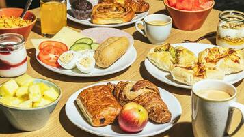 Una mesa de desayuno con diversas opciones de comida, como cruasanes, huevos y fruta.