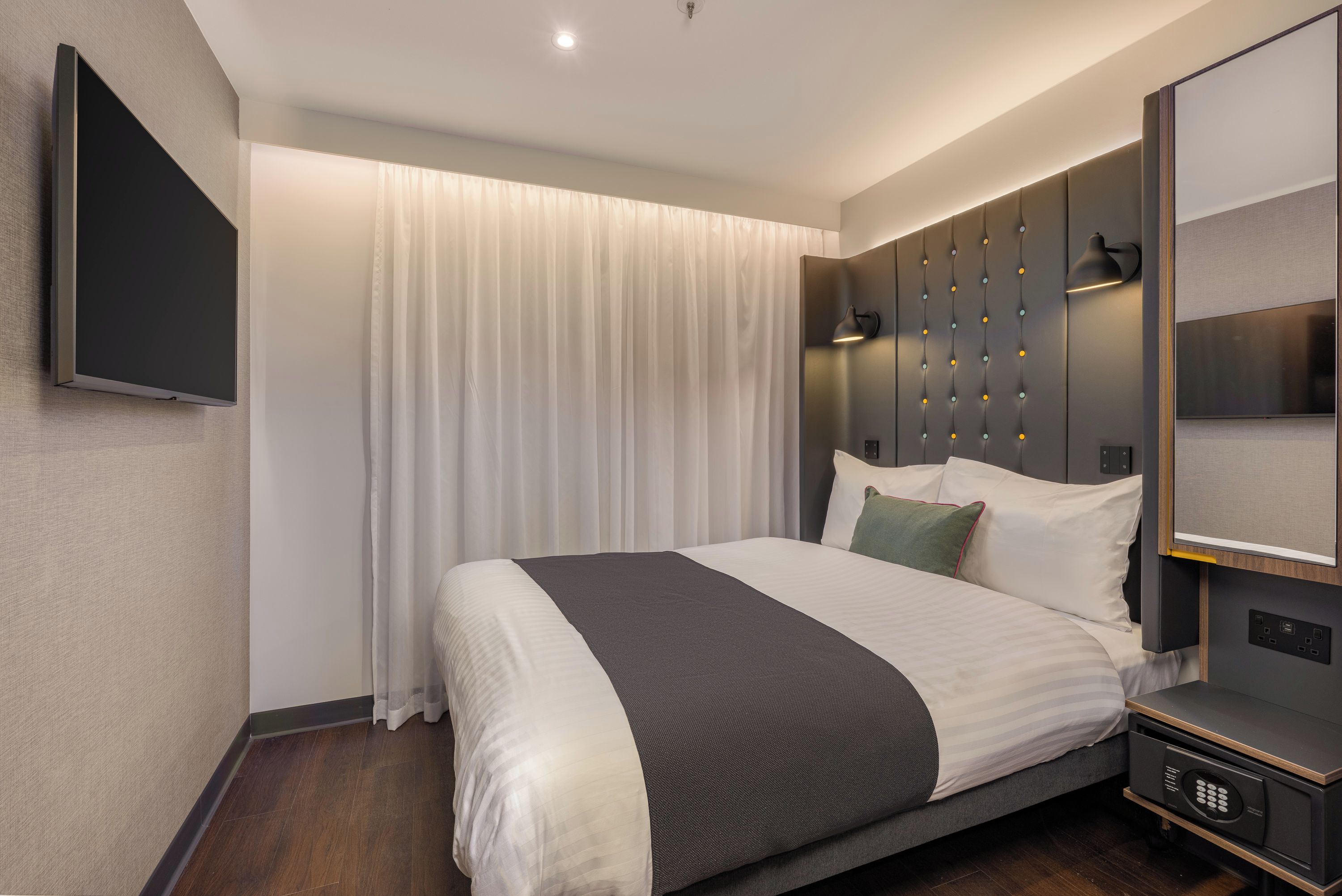 Een moderne hotelkamer met een groot bed, een flatscreen televisie, een nachtkastje met lamp en een bedieningspaneel.