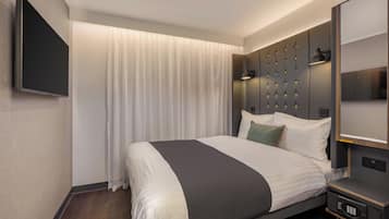 A modern hotel room with a large bed, a flat-screen TV, a bedside table with a lamp, and a control panel.