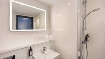 A bathroom with a white sink, a mirror with a light, a shower, and a blue door.