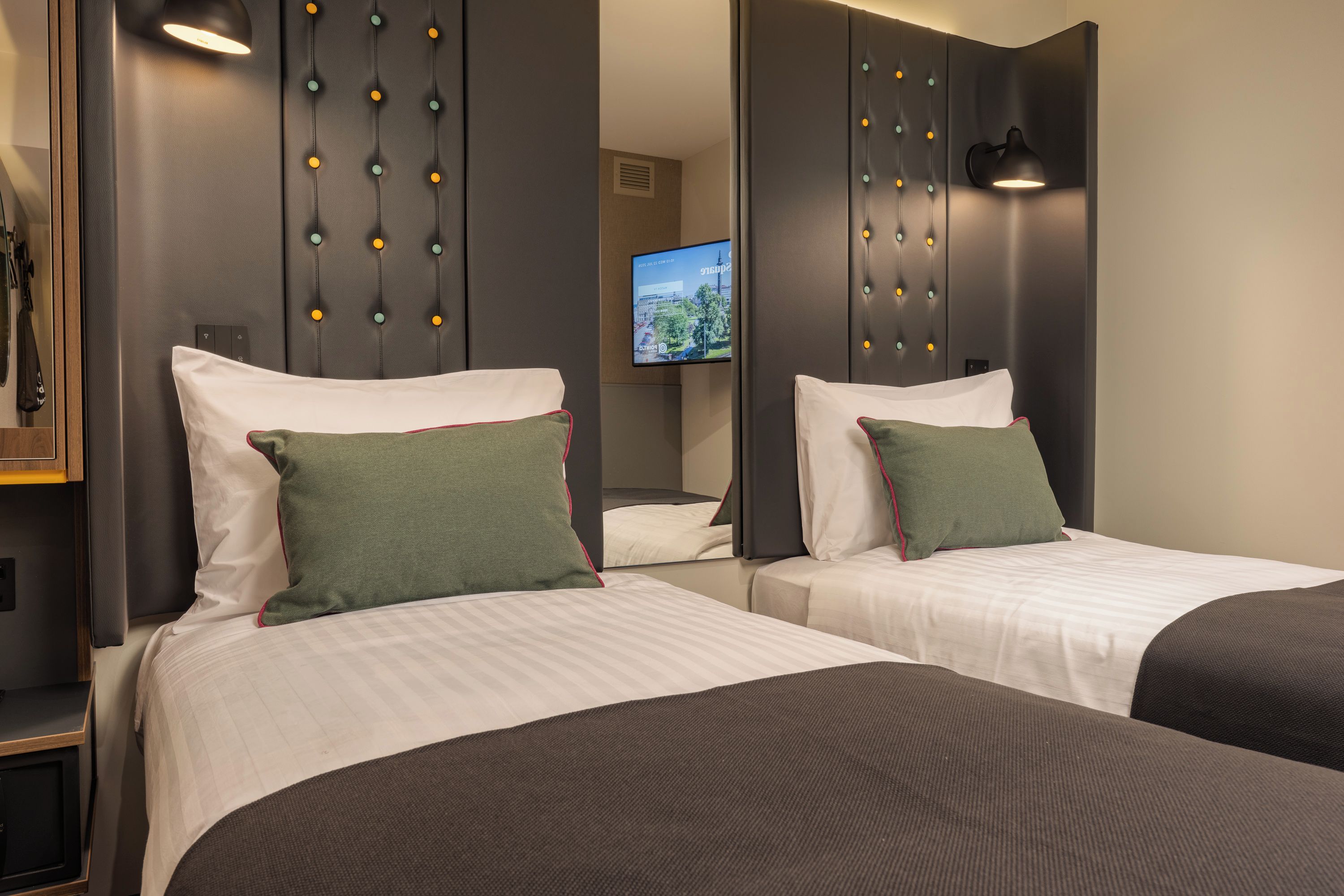 A hotel room with two beds, each with a pillow and a headboard with a light fixture.