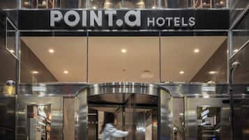 Der Eingang eines Hotels mit Glasfassade, einem Schild mit der Aufschrift 'POINT.A HOTELS' und einem Aufzug.