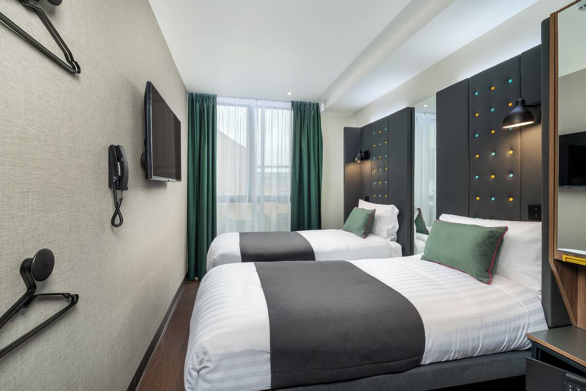 Hotellihuone, jossa on kaksi sänkyä, televisio, puhelin ja peili.