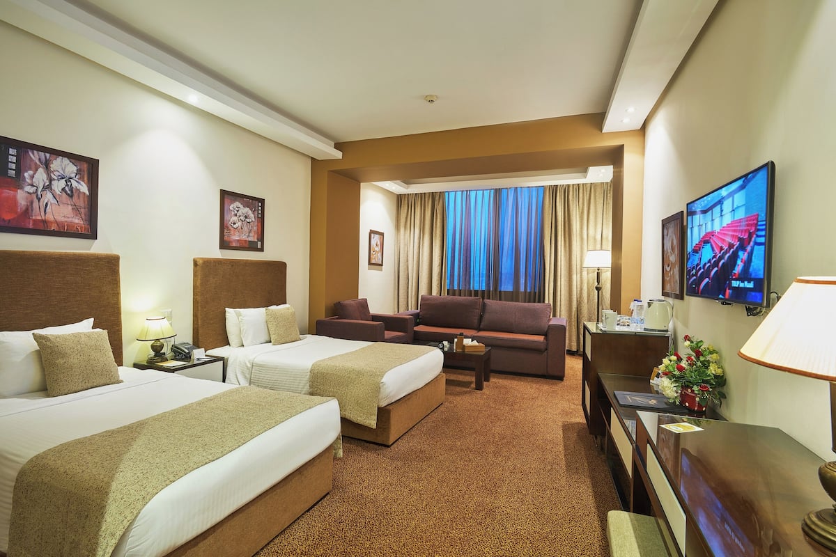 Habitación de hotel con dos camas, un sofá, un televisor y un escritorio con lámpara.