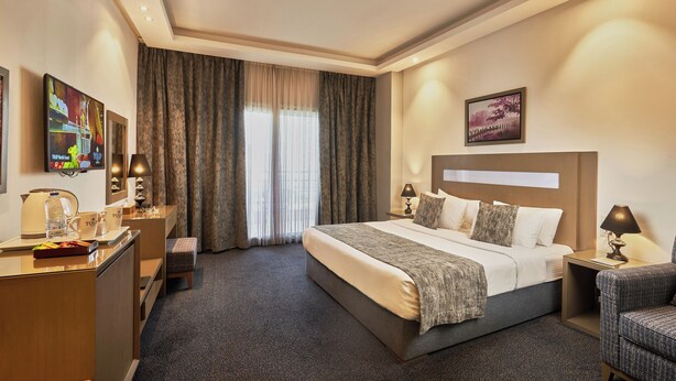 Una habitación de hotel con una cama grande, un escritorio con lámpara, una silla, un televisor y un cuadro en la pared.